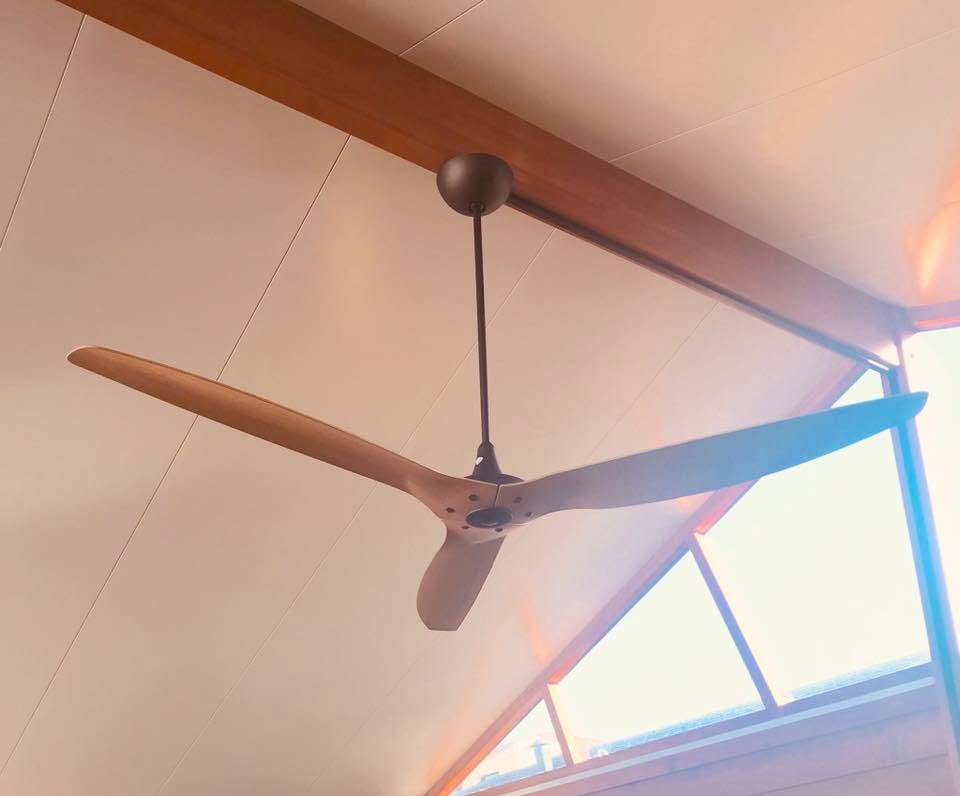 A timber-bladed ceiling fan on a raked residential ceiling with clerestory windows.