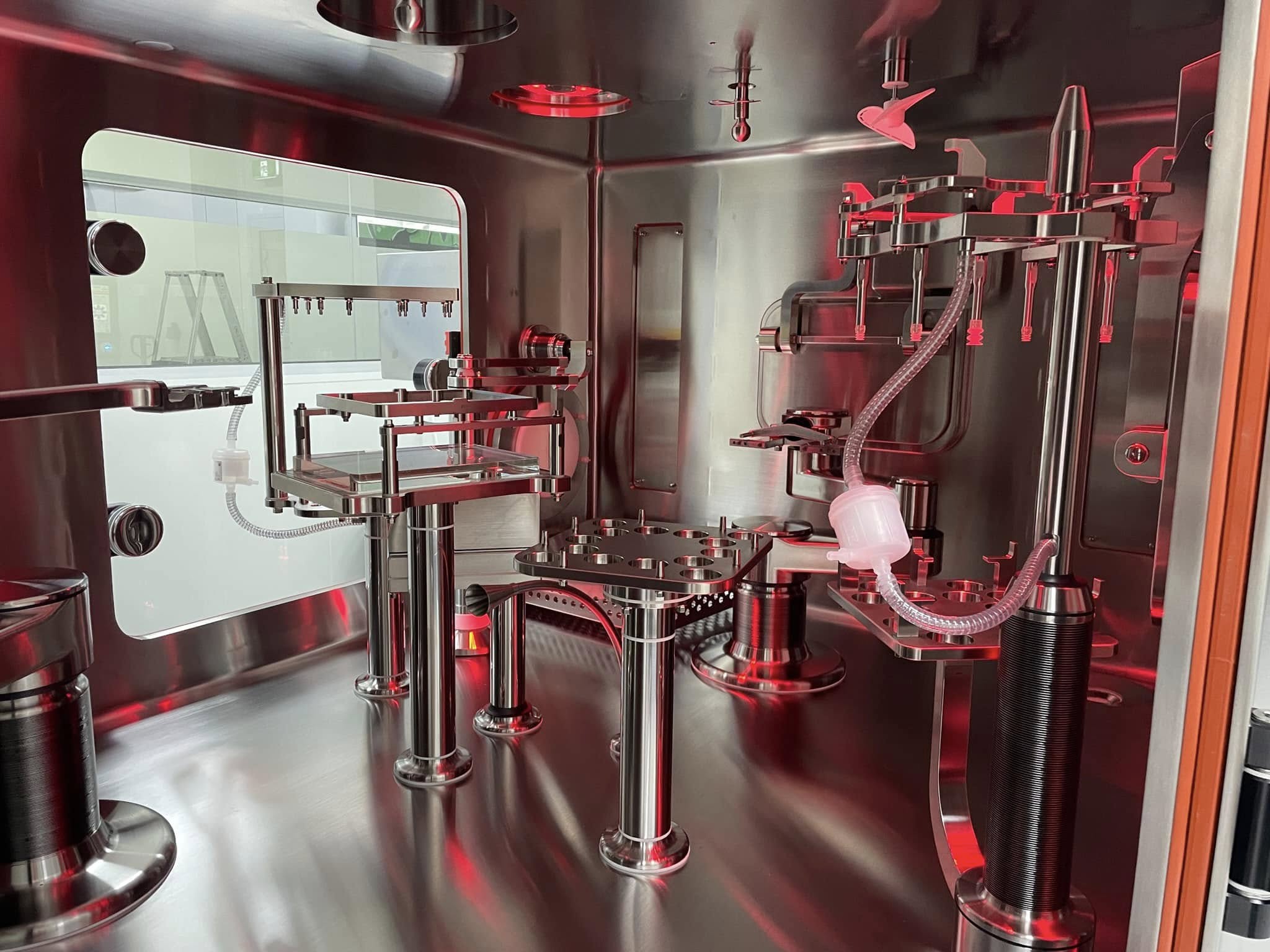 Stainless isolator and process vessel under red light inside the Biocina cleanroom.