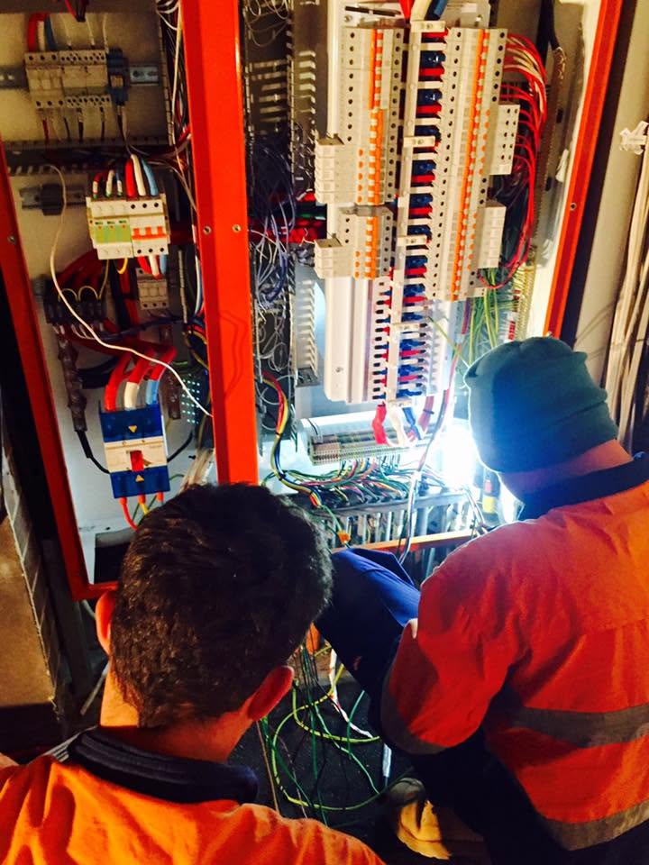 Two Oasis electricians in hi-vis terminating a panel.
