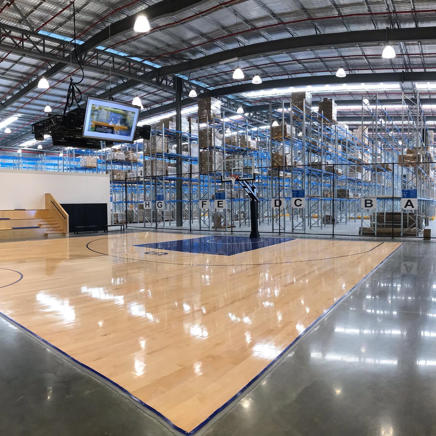 A polished basketball court set inside a distribution centre among high-bay racking, lit by LED high-bay fittings.
